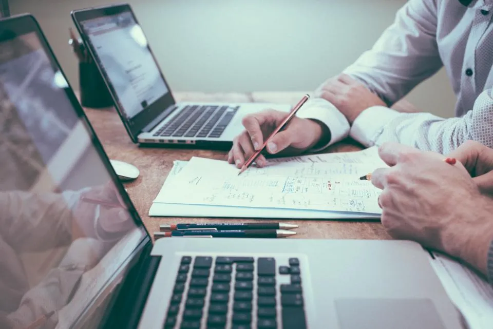 Deux personnes travaillent sur des documents et un ordinateur portable