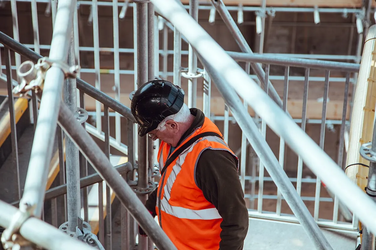 Un ouvrier en gilet orange et casque, au milieu des tubes d’un échafaudage